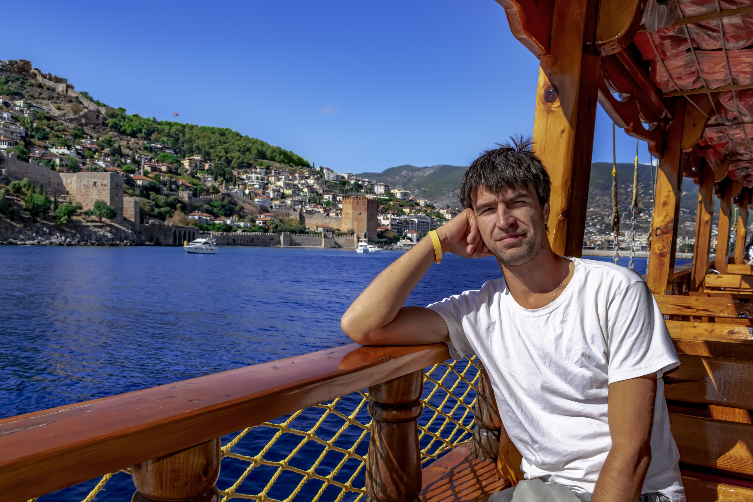 happy smiling man sits on the deck of a wooden boat against the backdrop of the landscape of alanya happy smiling man sits on the deck of a wooden boat against the backdrop of the landscape of alanya