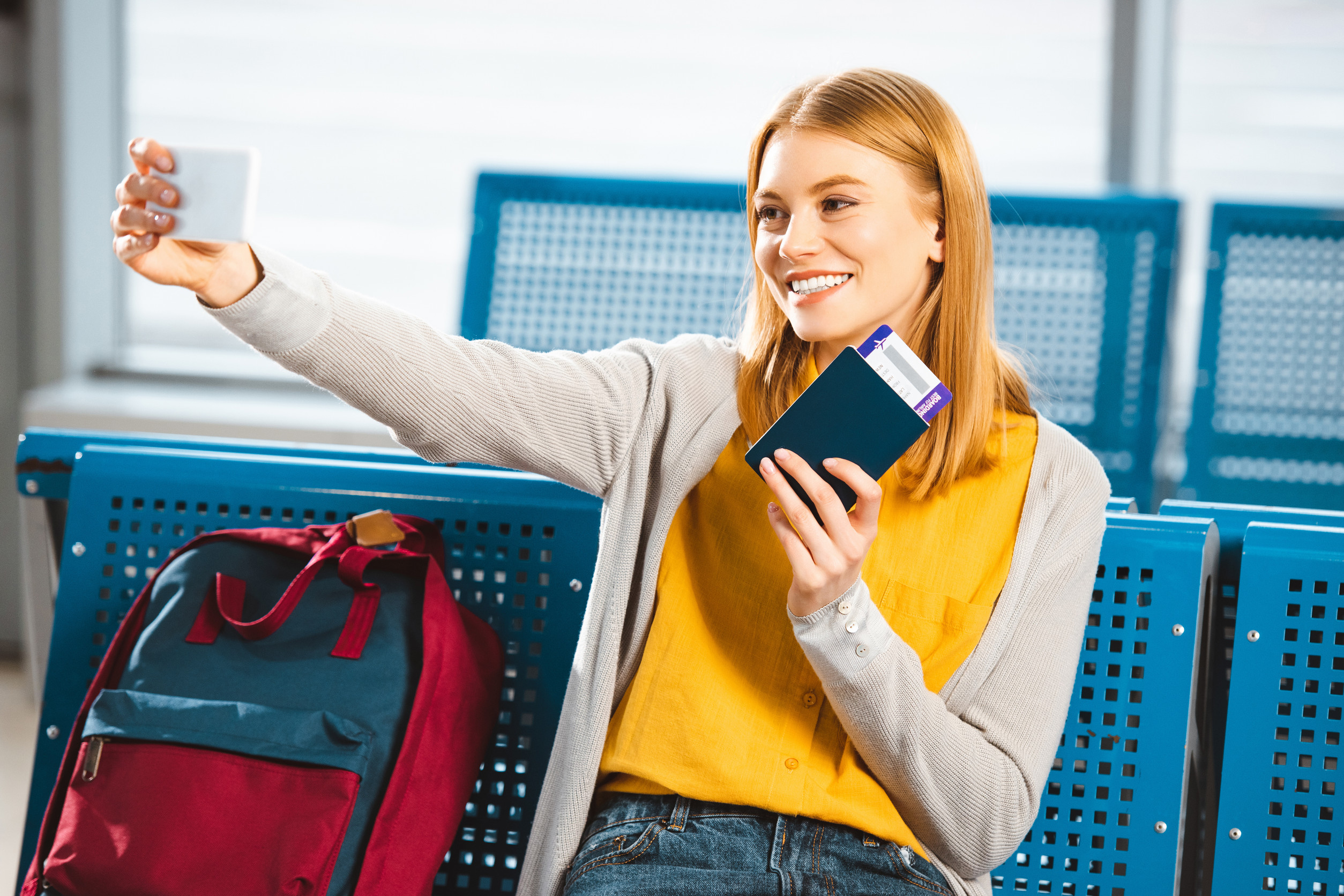 Smiling woman taking selfie with passport and air ticket in waiting hall Smiling woman taking selfie with passport and air ticket in waiting hall