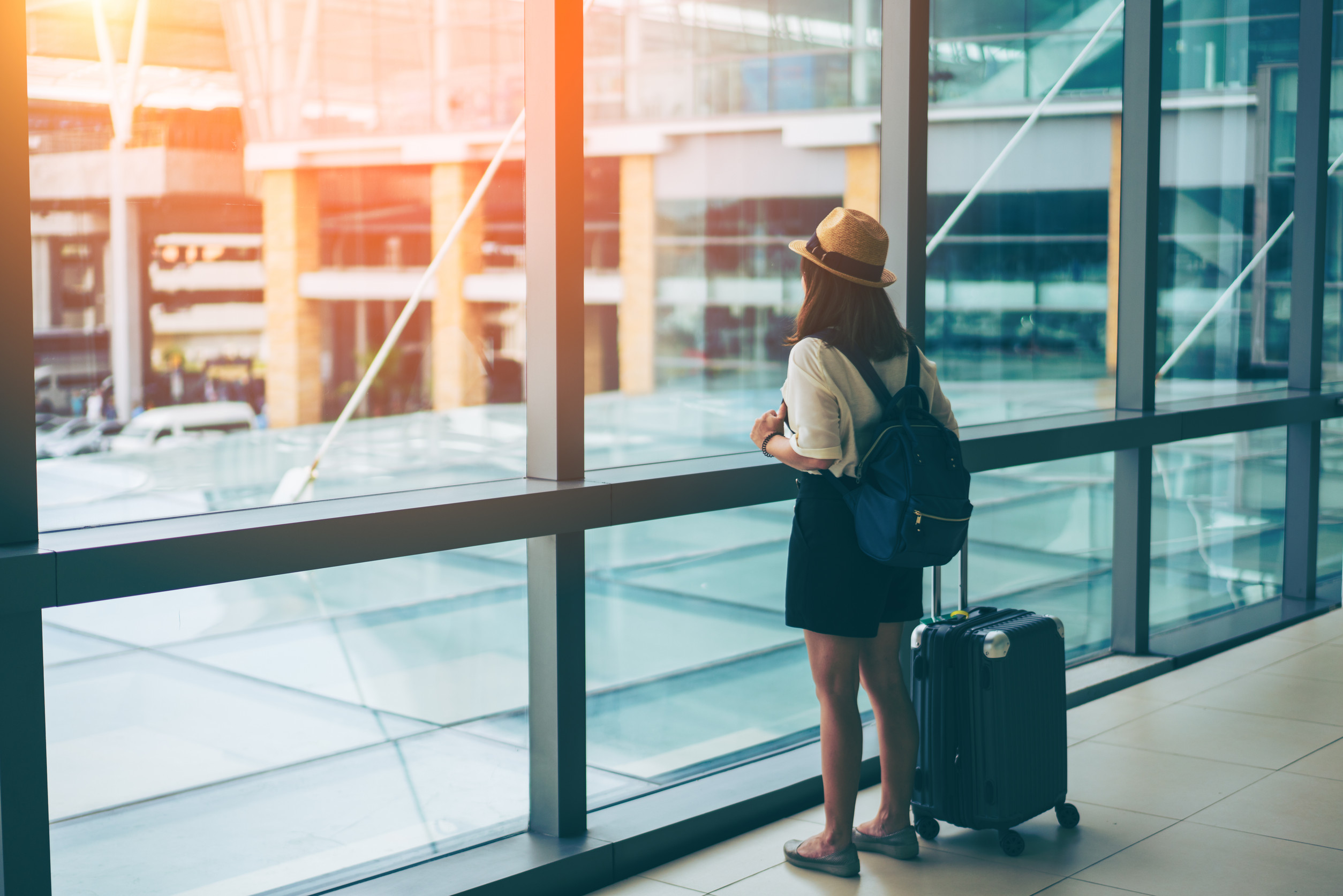 young asian woman with baggage looking through the window of an airport departure young asian woman with baggage looking through the window of an airport departure